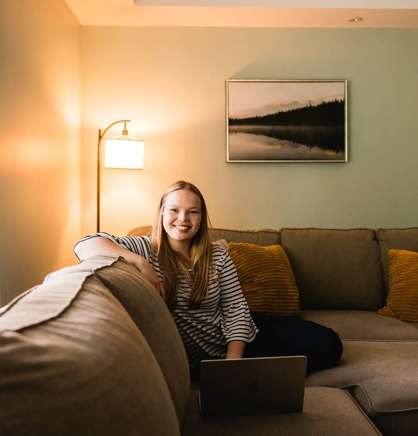 Nicole Graff-Rowe smiles from her couch in a warmly lit living room, a laptop beside her.