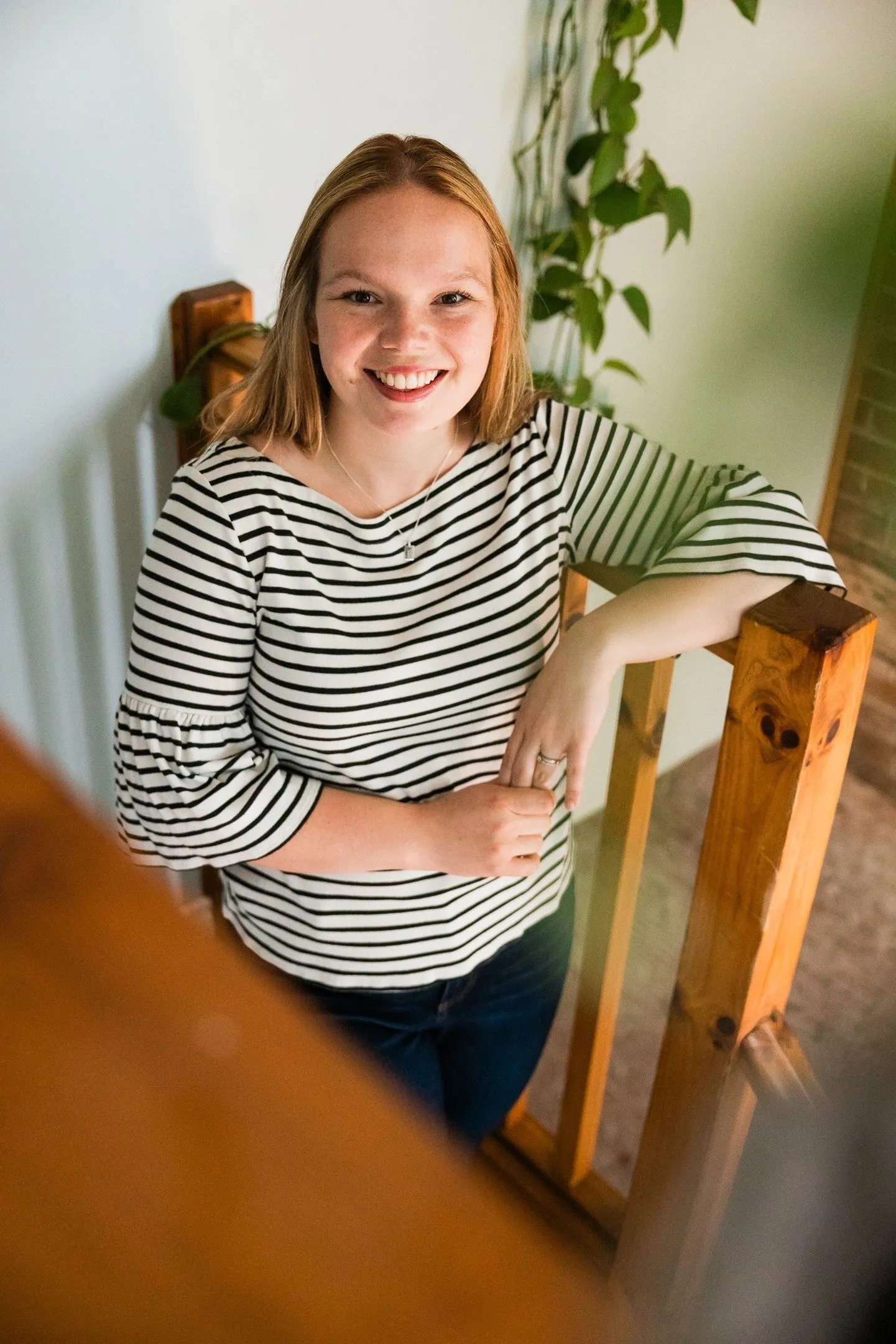 Nicole Graff-Rowe leans on a wooden stair railing at home, smiling.