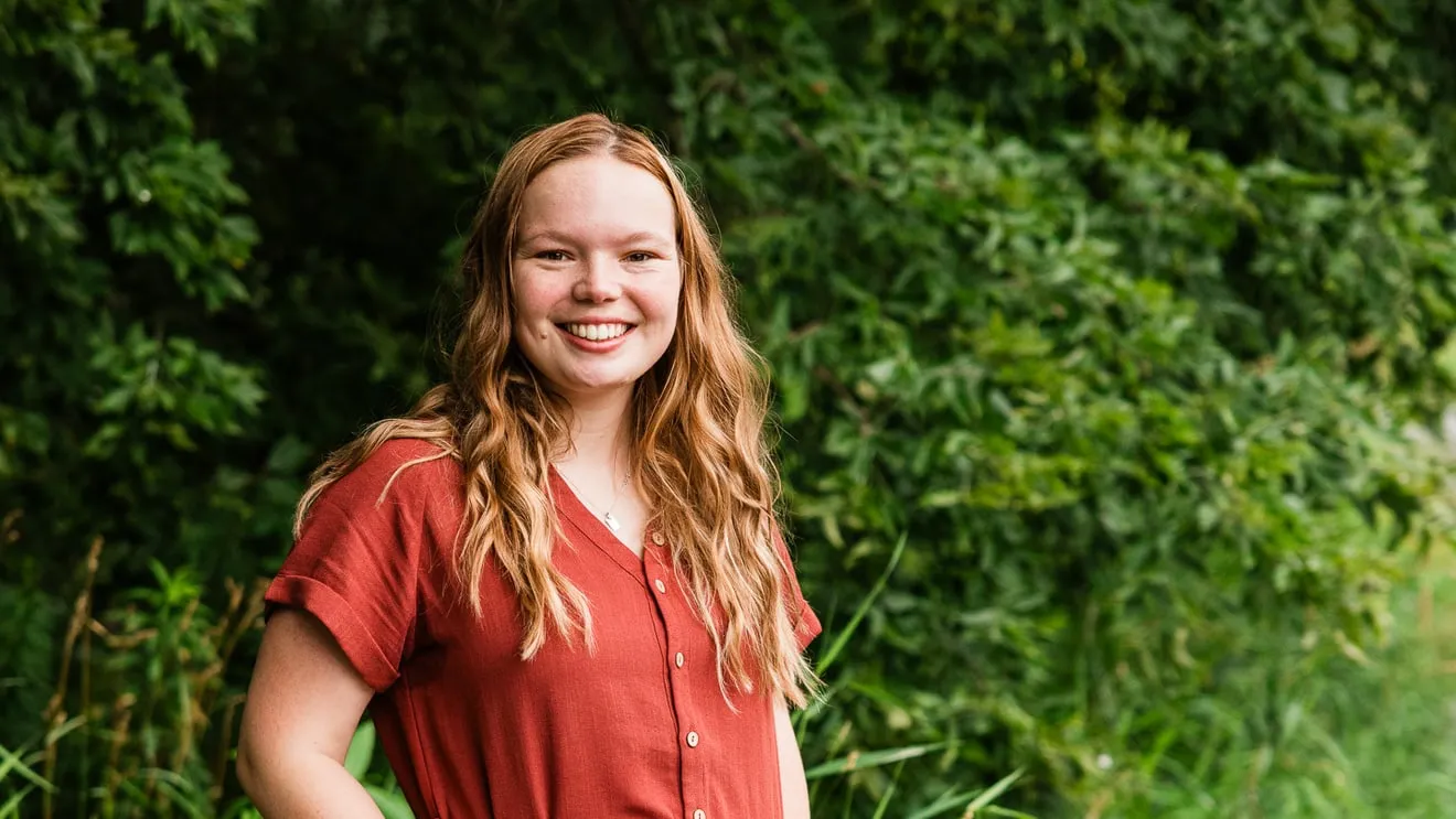 Nicole Graff-Rowe smiling outdoors in front of green leaves.