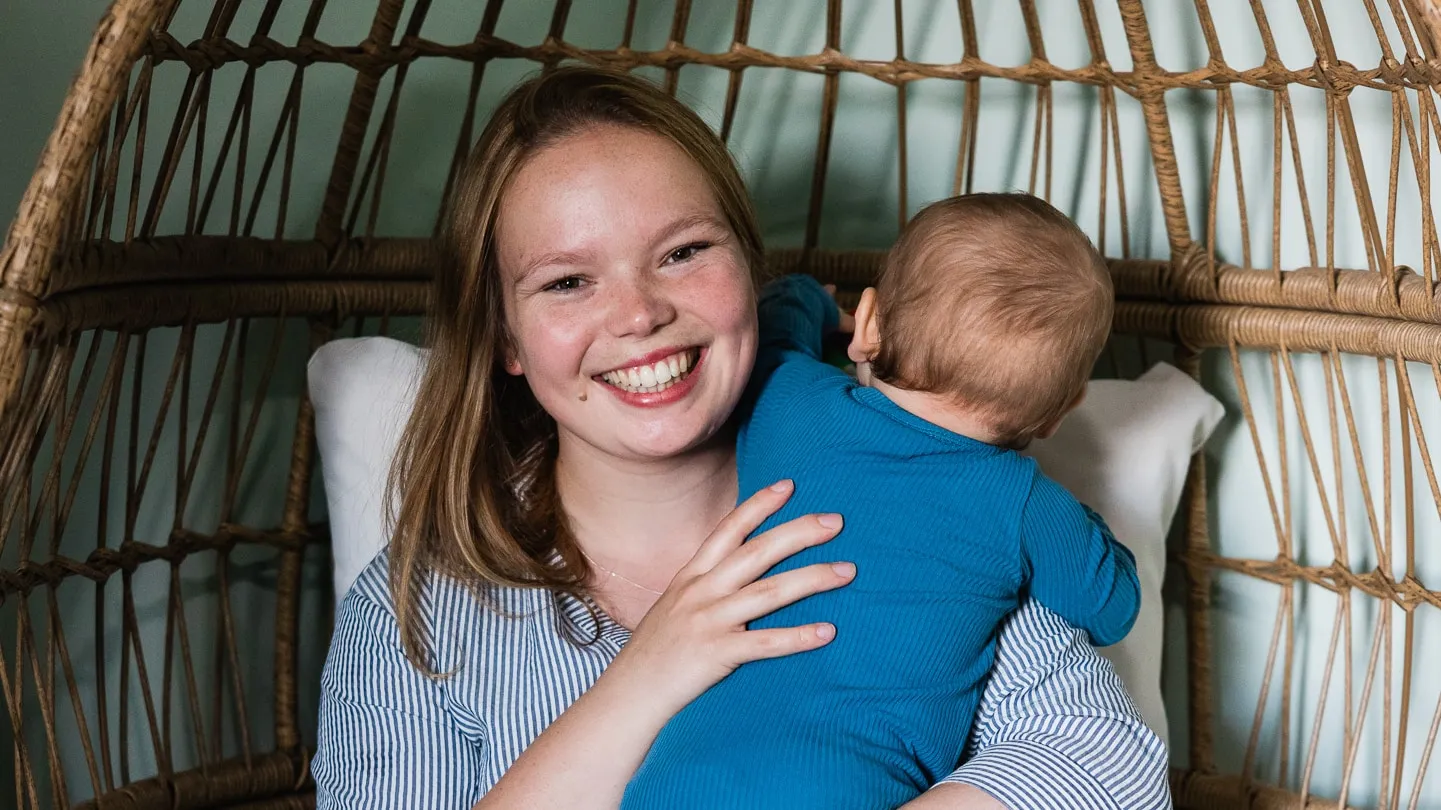 Nicole Graff-Rowe smiling in a wicker chair, holding her baby