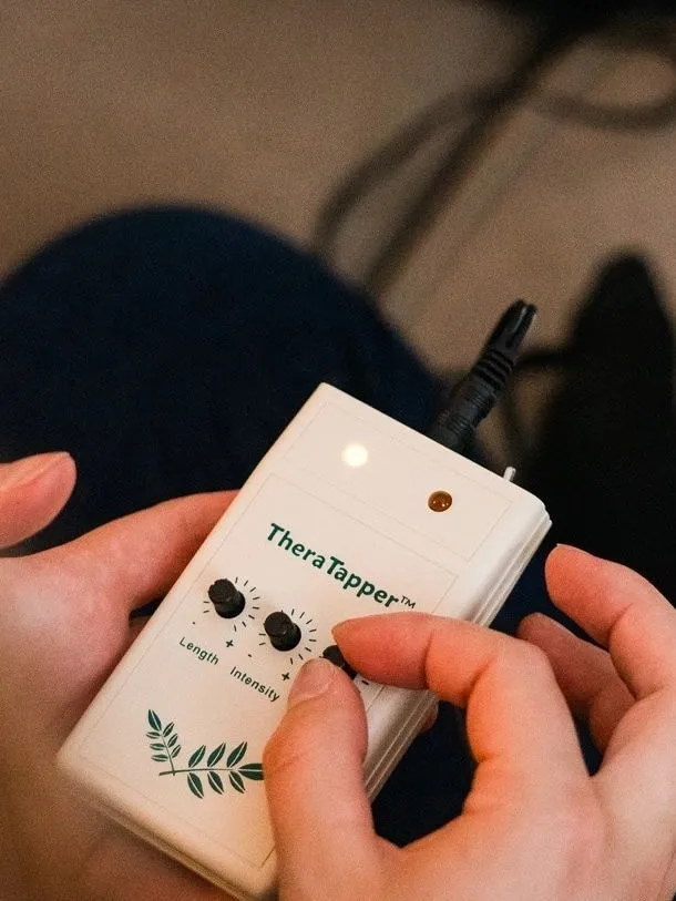 Hands hold a TheraTapper, a small device that sends gentle alternating taps during EMDR therapy.